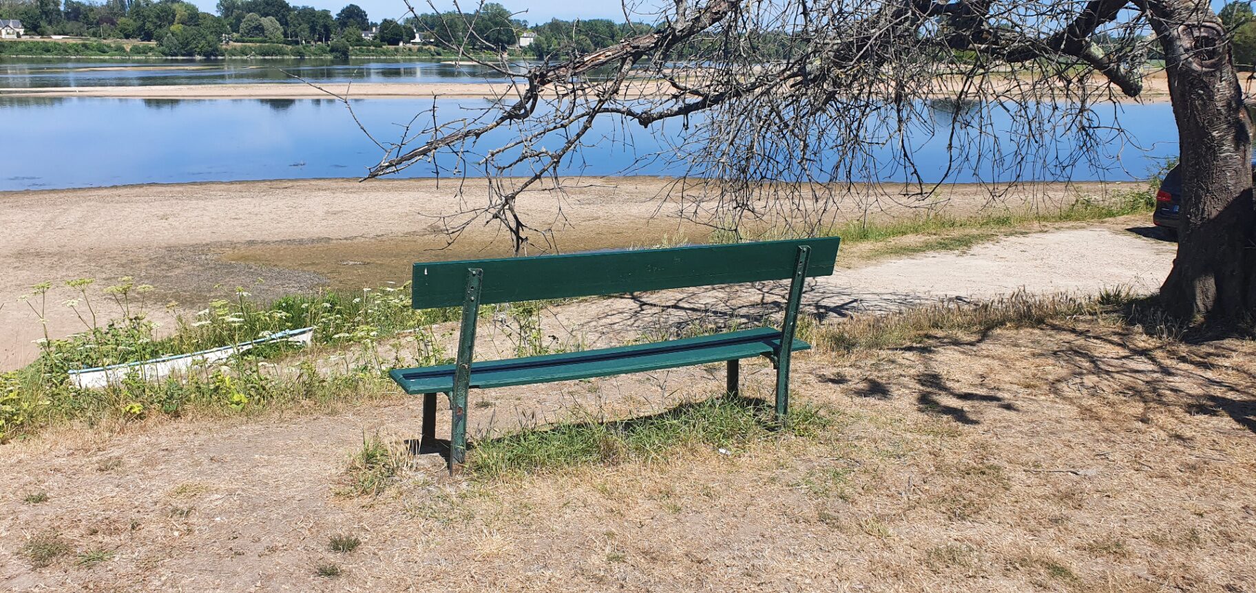 An empty green bench beside a wide, low river — a seat left open, the kind of place a conversation might continue.