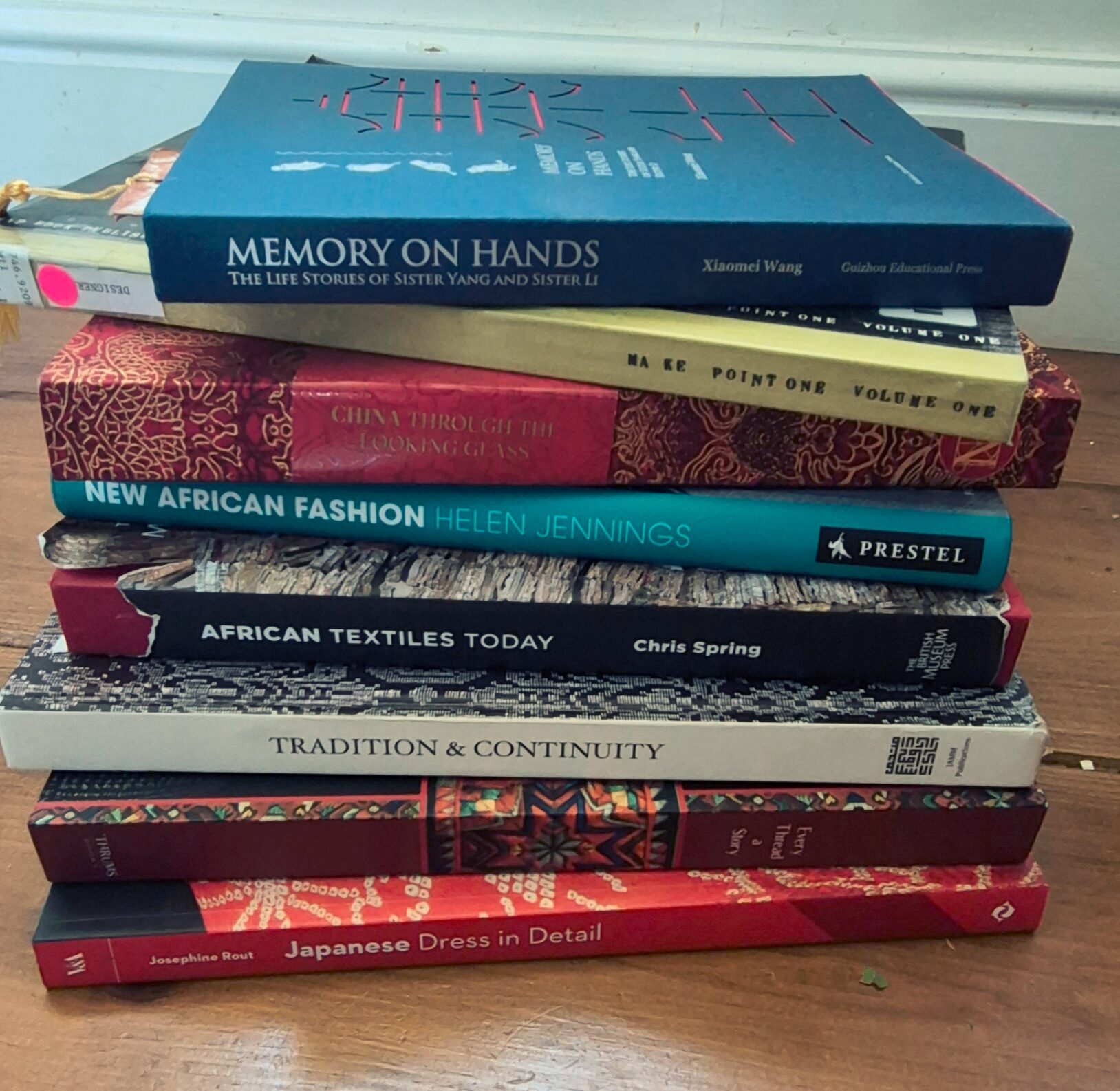 A stack of international books on textiles, culture and design resting on a wooden surface.