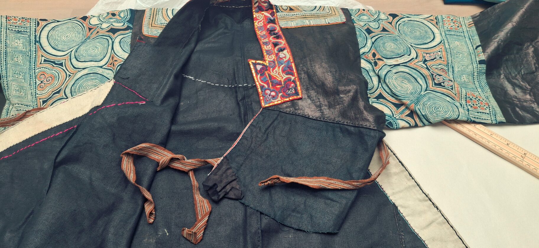 A hand-embroidered Chinese silk garment laid flat, its collar, buttons and stitched detail fully visible.