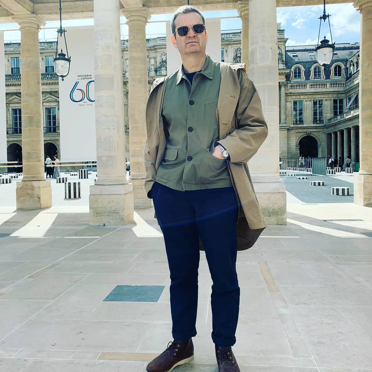 A person standing in the Palais Royal courtyard in Paris, with stone columns and a Ministry of Culture banner behind them.